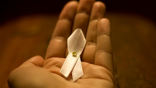 A hand holding a White Ribbon Day ribbon.