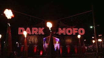 Neon red lights reading "Dark Mofo" amid pyramids shooting out fire.