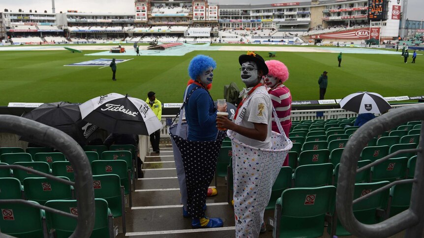 Spectators dressed as clowns wait for play to start as rain falls during day four at The Oval.