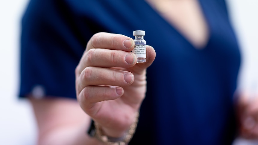 A close up of a hand holding a small vial with a Comirnaty label