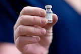 A close up of a hand holding a small vial with a Comirnaty label