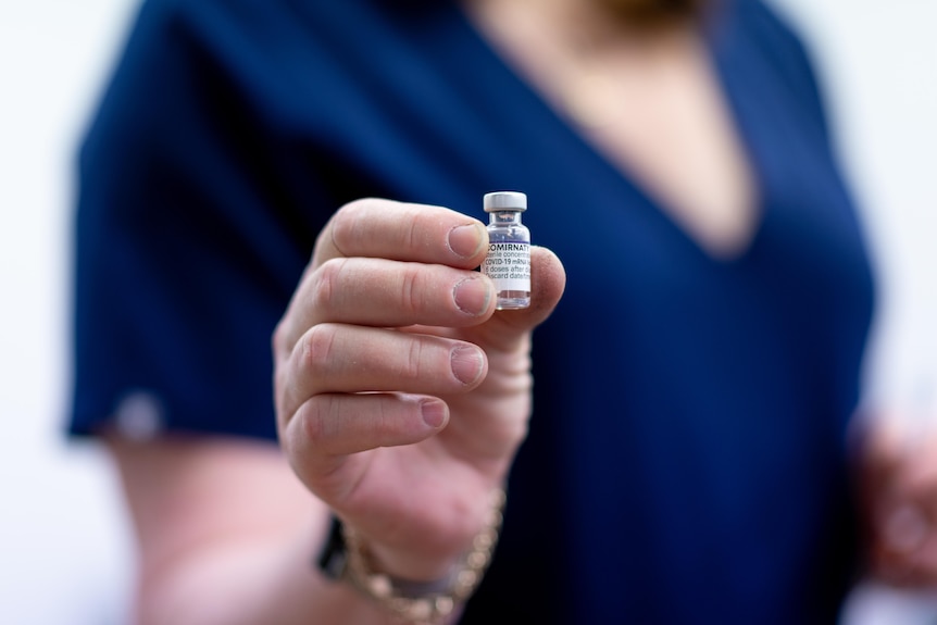 A close up of a hand holding a small vial with a Comirnaty label