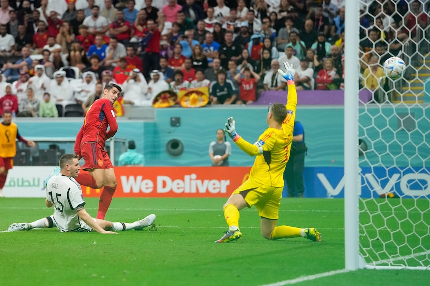 A Spanish striker looks up at the goal as his shot flies past the goalkeeper into the net.