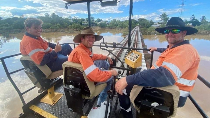 three men in high vis drive a train while smiling at the camera 