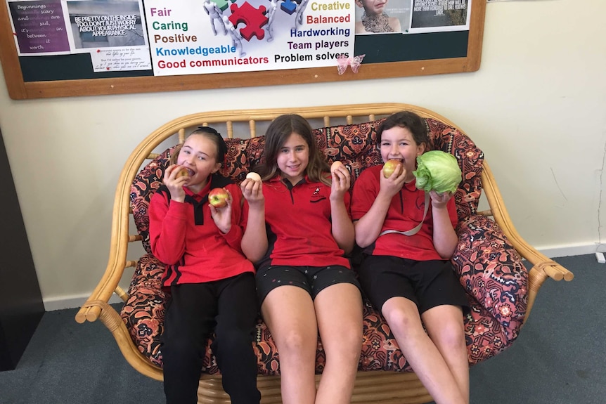 Three smiling school girls enjoying a healthy snack.