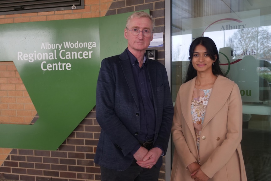 man in suit and glasses stands next to young woman, in front of albury wodonga regional cancer centre sign