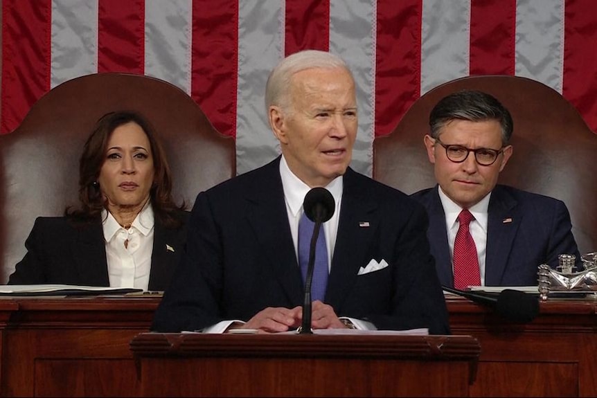 Joe Biden delivers State of the Union at a podium. Vice President Kamala Harris and House Speaker Mike Johnson sit behind him.