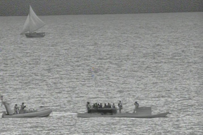 Indonesian fisherman are intercepted by border security with a sailing boat in the background.