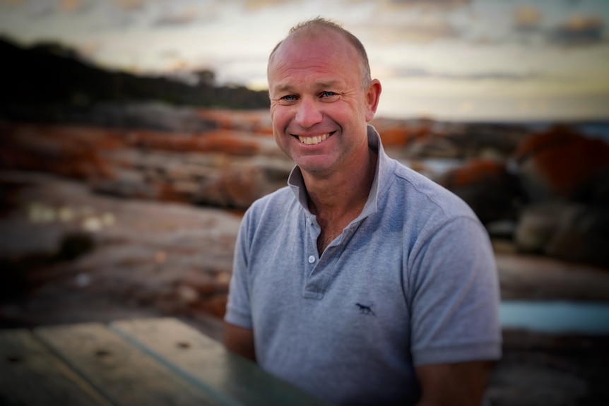 Renison Bell smiles for the camera, with the craggy Tasmanian coastline behind him.