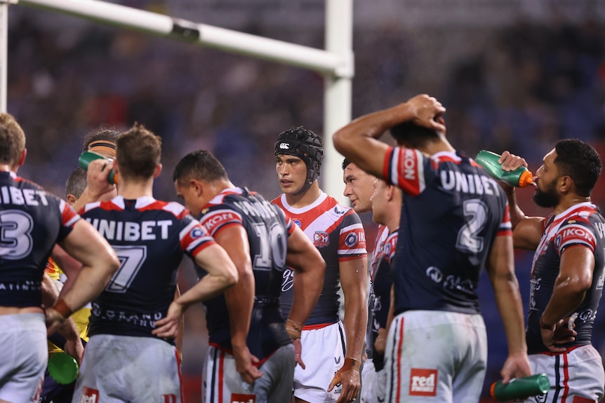 Joseph Suaalii of the Sydney Roosters, wearing headgear, stands with his teammates after conceding an NRL try against the Storm.