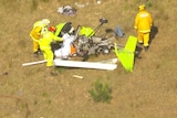 An aerial view of the wreckage of a small, green aircraft on grass with people in high-vis walking around it.
