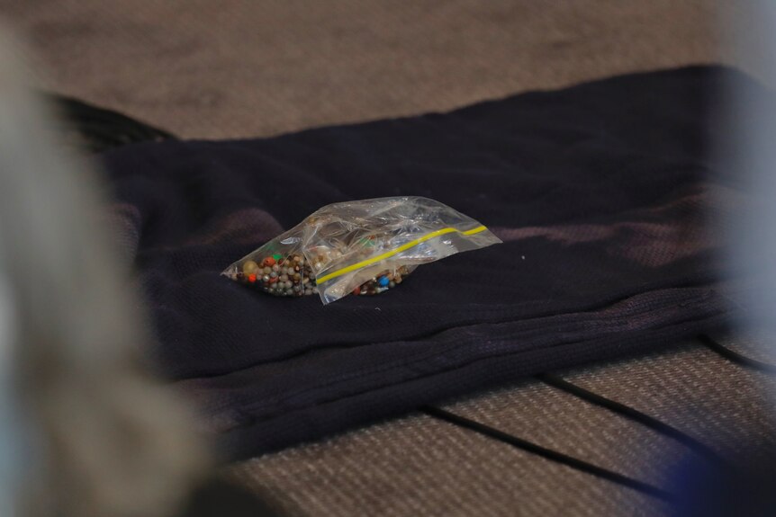 A shot of some plastic beads in a bag sitting on top of a blanket lying on the ground.