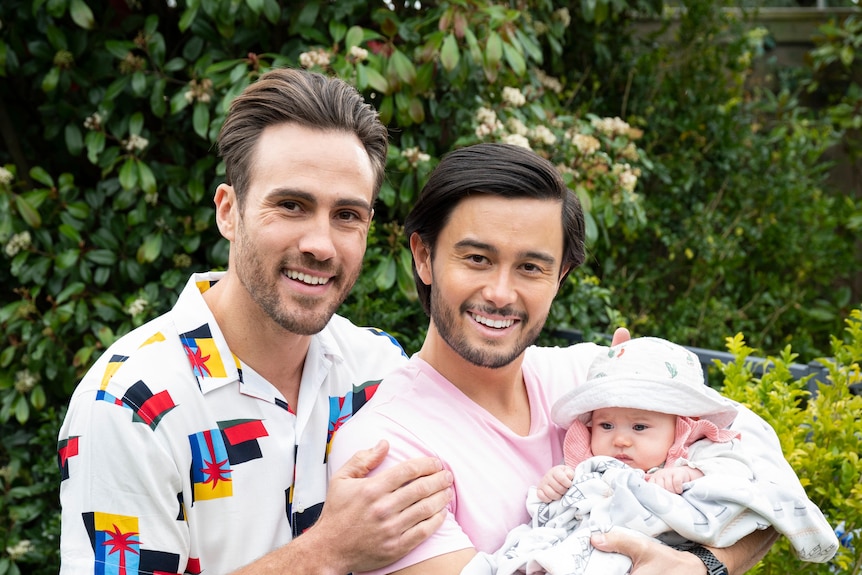 Two men smile and hold a baby.