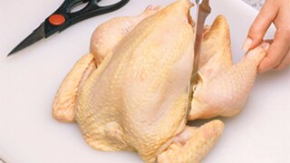 A woman cuts into a whole, uncooked chicken using a knife.