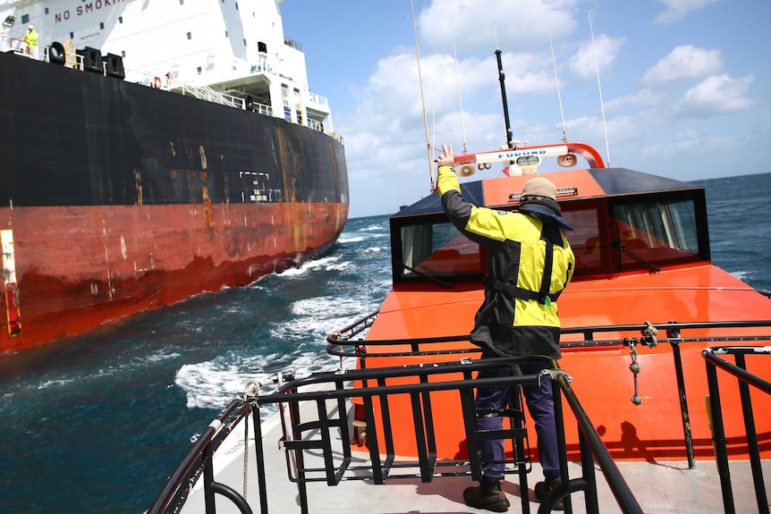 A man in a boat waves at a large container ship.