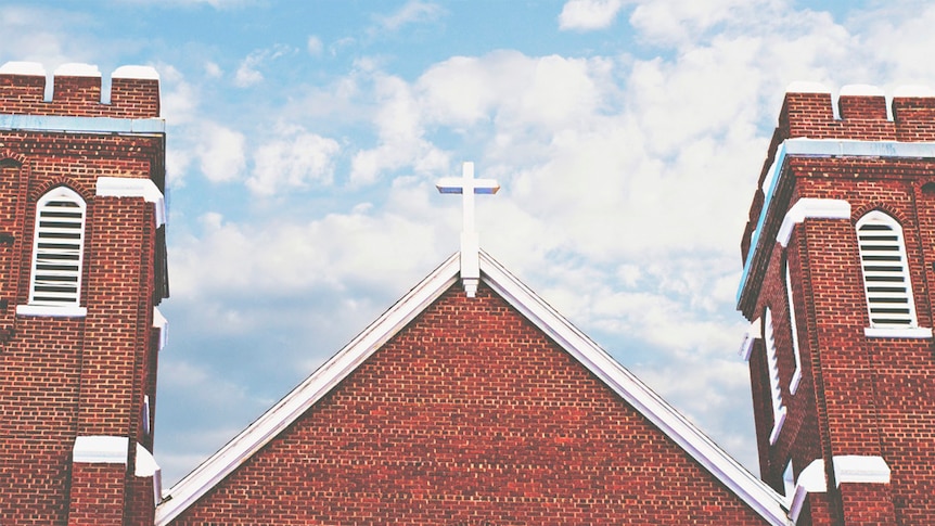 A cross sits atop a red brick church building.