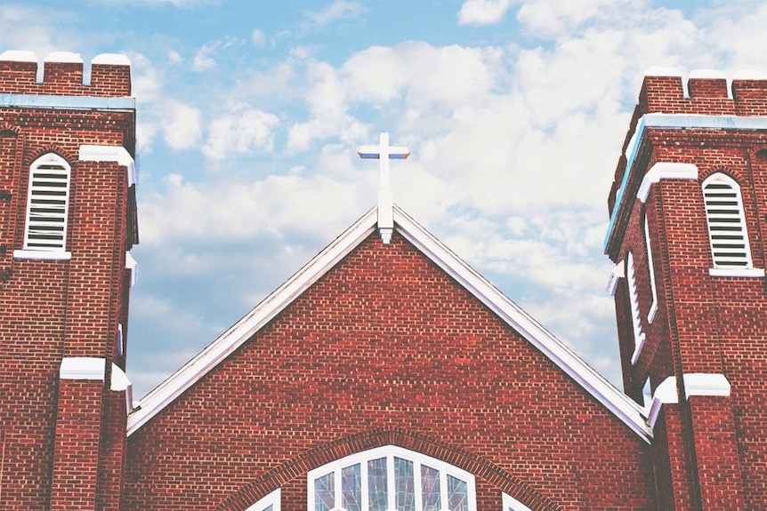 A cross stands atop a red brick church building.