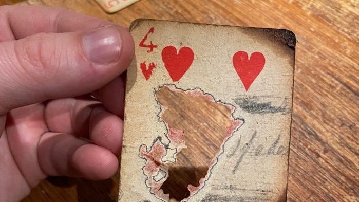 an old four of hearts playing card that is burnt around the edges and a hole in the middle