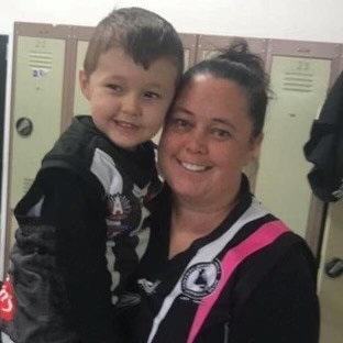 A woman smiling holding a smiling young boy in front of a group of lockers  
