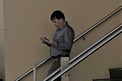 A man holding his phone and walking down the stairs outside a courthouse.