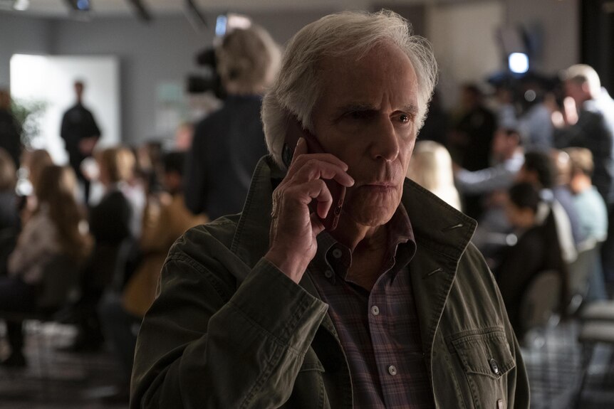 Henry Winkler on the phone in front of a crowd of people.