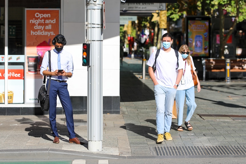 Tow men and a woman waiting a the lights wearing masks