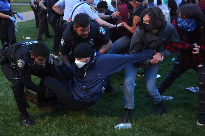 Two police grab a protester who is on the ground as two other protesters pull him by his arm