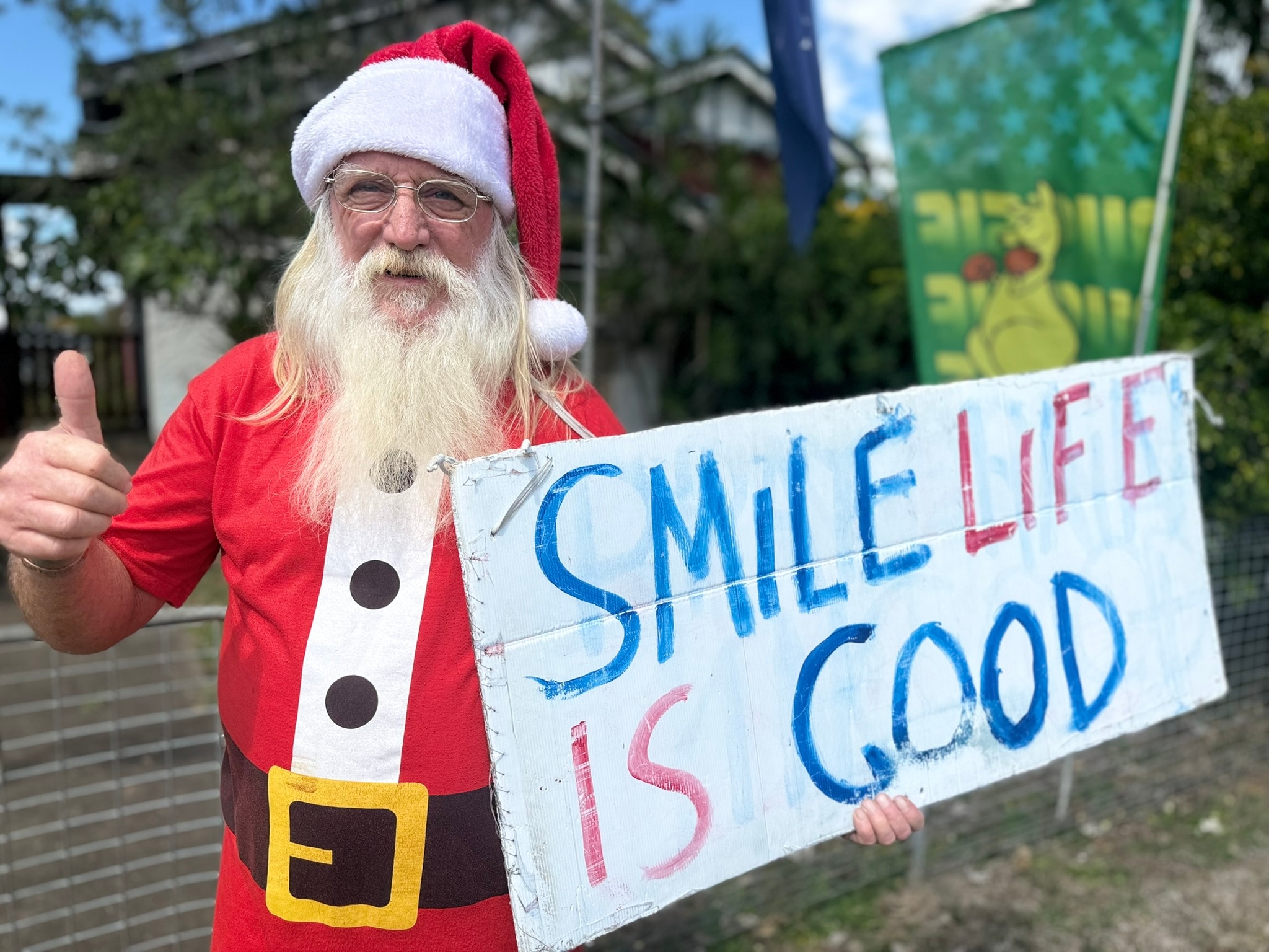 A man dressed as Santa holds up a sign reading Smile Life Is Good