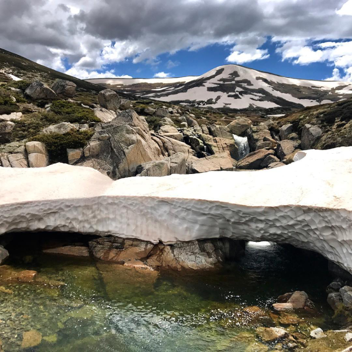 A creek flows between a snowy bridge on a mountain side.