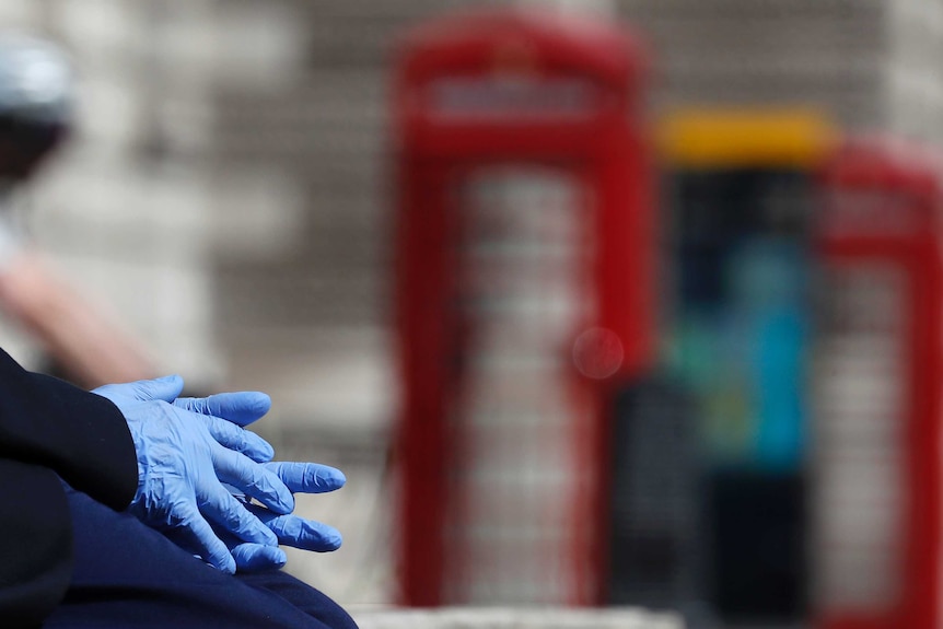blue rubber gloves are in focus, with a red telephone box blurred in the background.