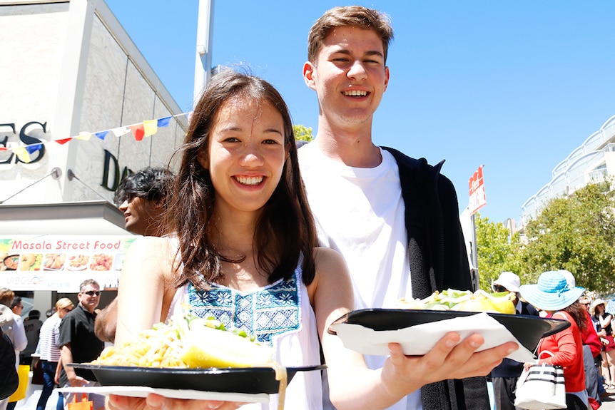 A woman and man holding pad thai on plates.