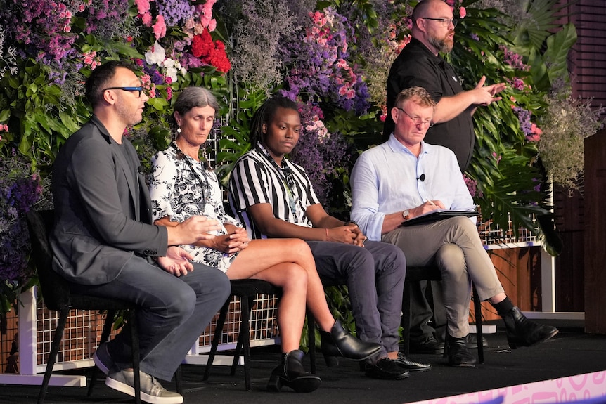 Four people sit in chairs on stage, one person is speaking while the others are listening.