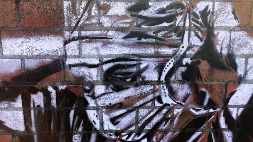 Stencil art on a brick wall depicting a healthcare worker strapping on a face mask