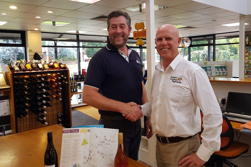 Two men stand in a tourist shop shaking hands.