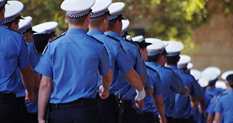Police recruits march in uniform with their backs turned in a graduation ceremony.
