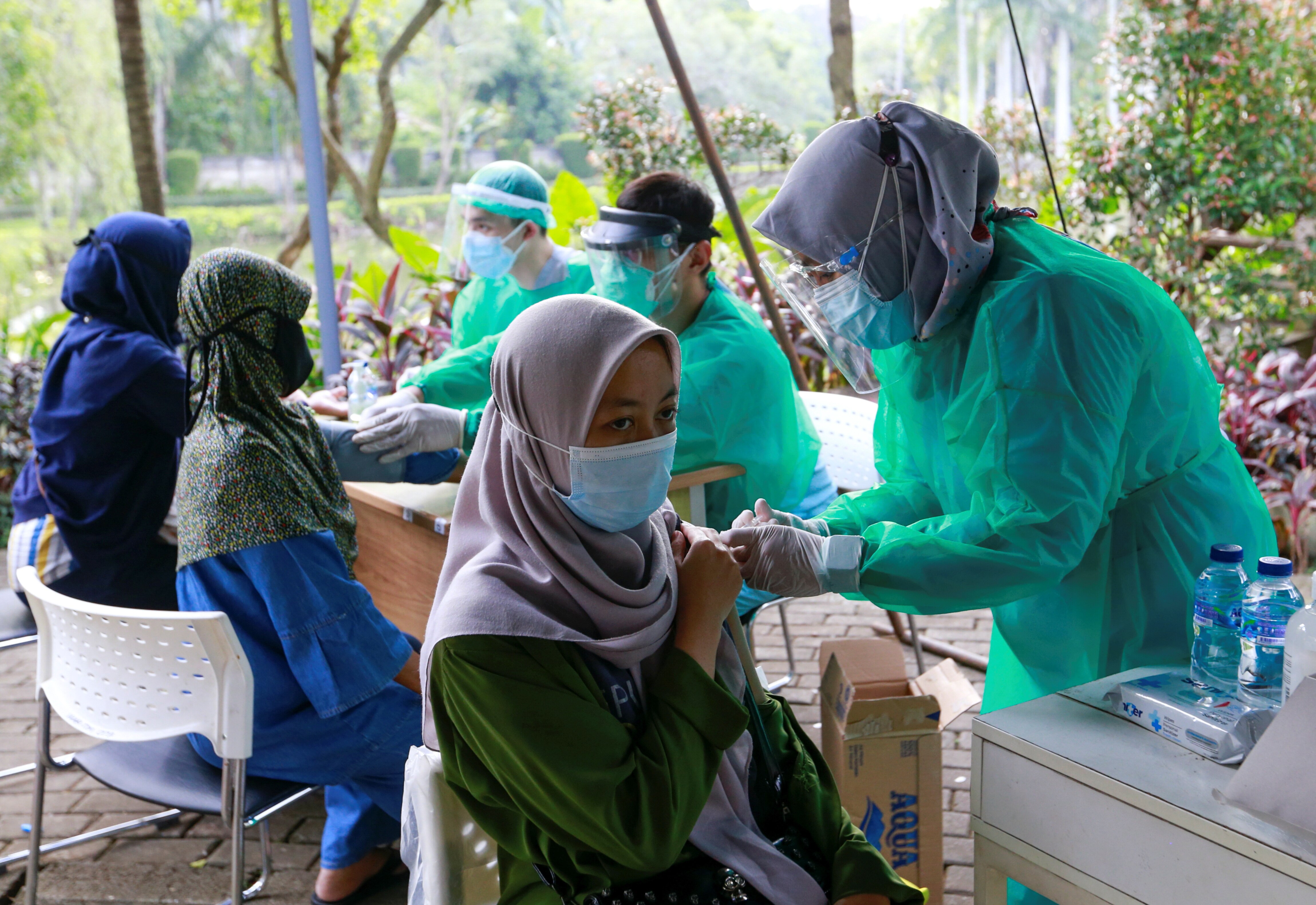 Three Asian women in Islamic headscarves get a COVID jab from nurses in full PPE, at an outside pop up clinic.