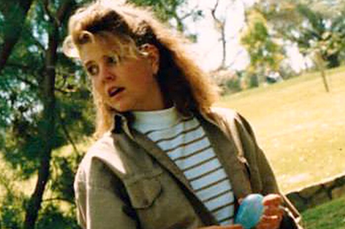 Jane Rimmer wearing a khaki jacket and white striped t-shirt, standing in a park.