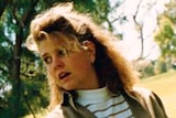 Jane Rimmer wearing a khaki jacket and white striped t-shirt, standing in a park.