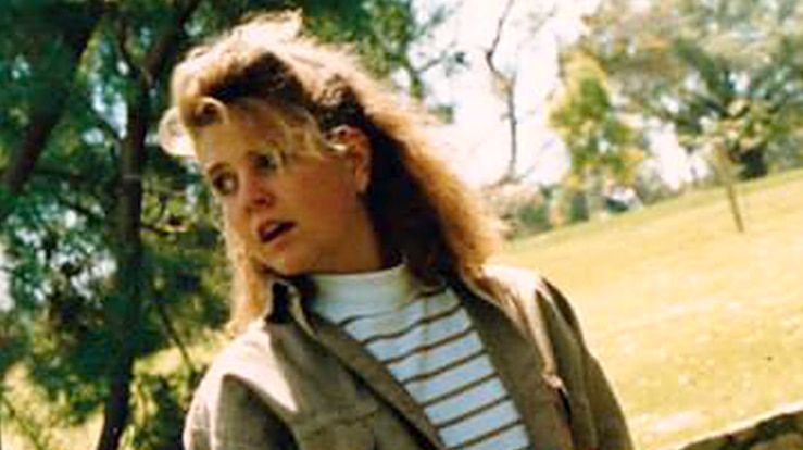 Jane Rimmer wearing a khaki jacket and white striped t-shirt, standing in a park.