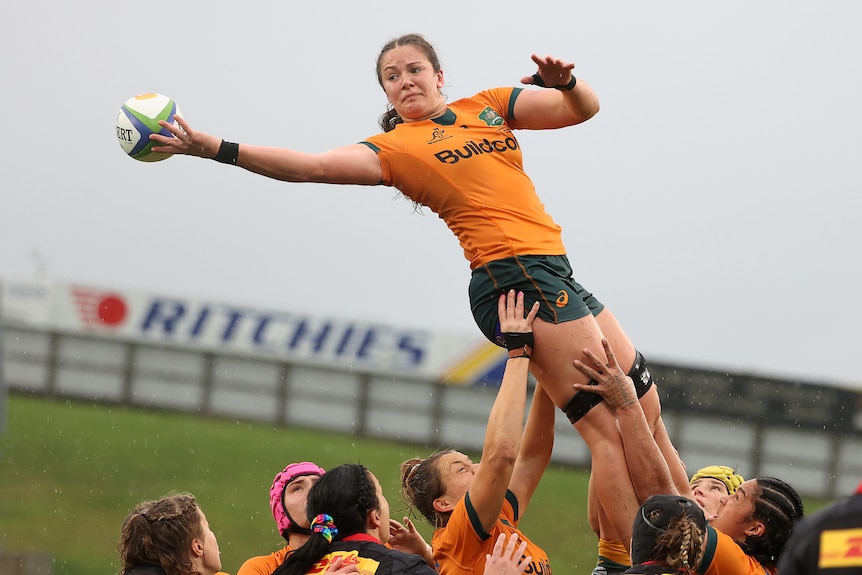 Michaela Leonard catches the ball with one hand after being lifted by a group of other players