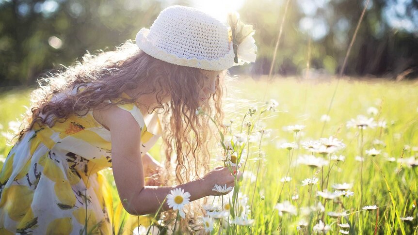 A young girl in a yellow dress picking flowers in a field
