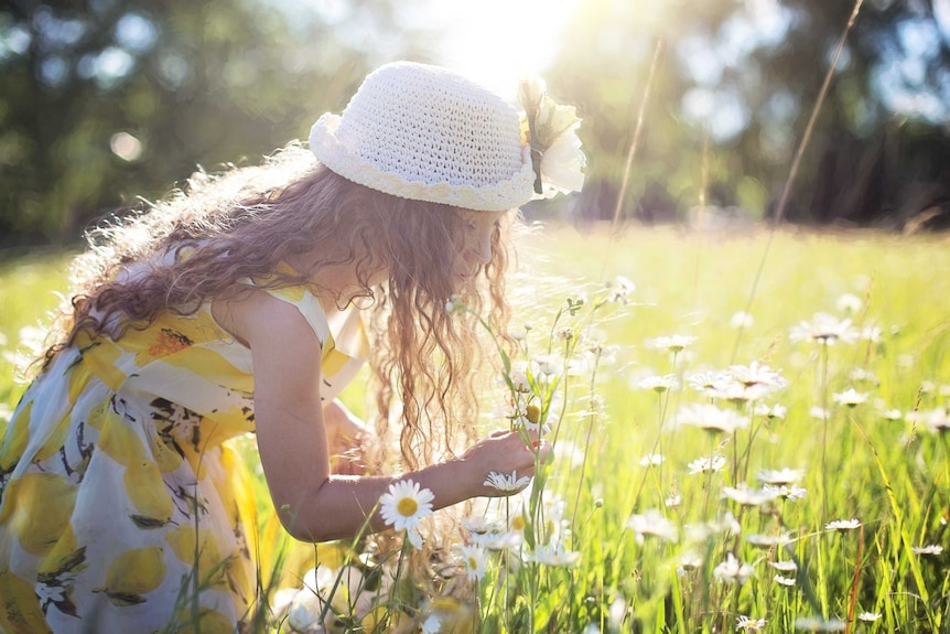A young girl in a yellow dress picking flowers in a field