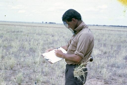 A man stands in a paddock writing on a notebook