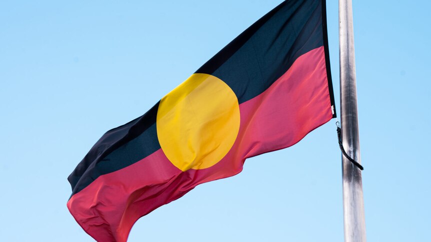 An Aboriginal flag flies on flag pole on a sunny day 