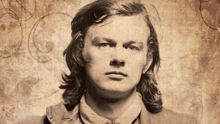 A sepia-tone image of Broderick Smith as a young man, with 70s shoulder-length hair and a steady gaze.