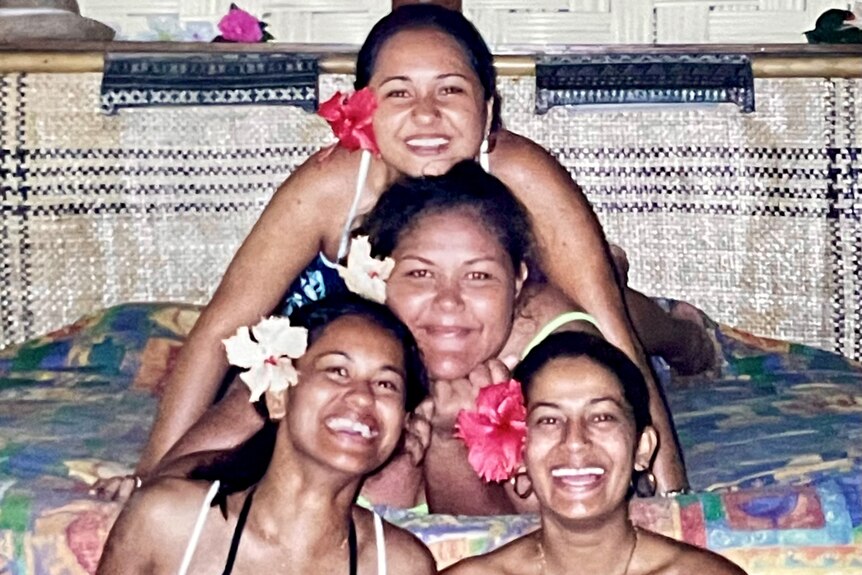 Four girls with flowers behind left ears sit in pyramid pattern and smile at camera.
