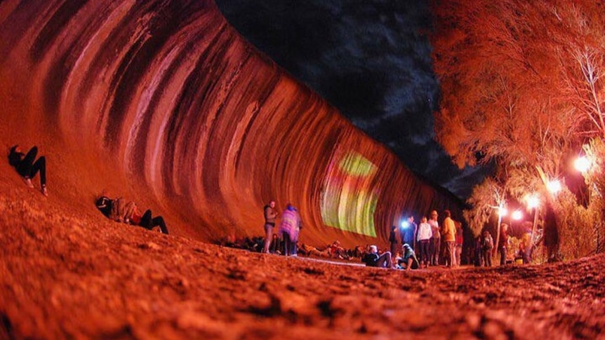 A giant red wave of rock with people nearby. 