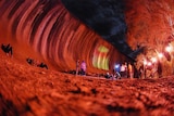 A giant red wave of rock with people nearby. 