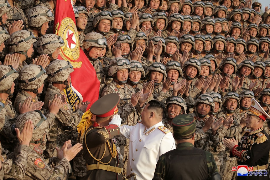 Kim Jong Un en veste blanche se tient devant une foule immense de parachutistes en uniforme 
