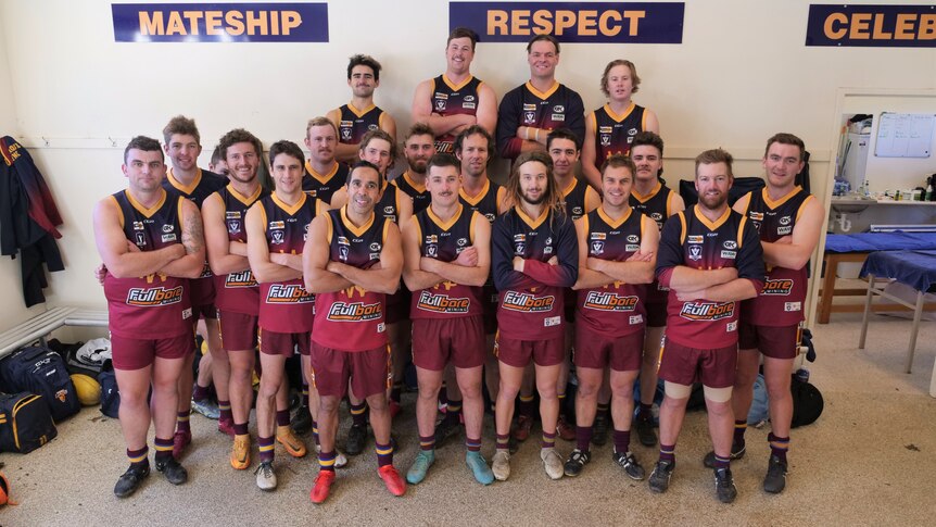 A group of football players gathered in a room posing for a photo, with the players including AFL legend Eddie Betts 